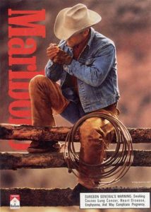 Marlboro cigarette ad featuring a cowboy sitting on a fence lighting a cigarette 