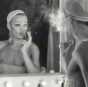 drag queen looking in the mirror with a blu e-cigarette