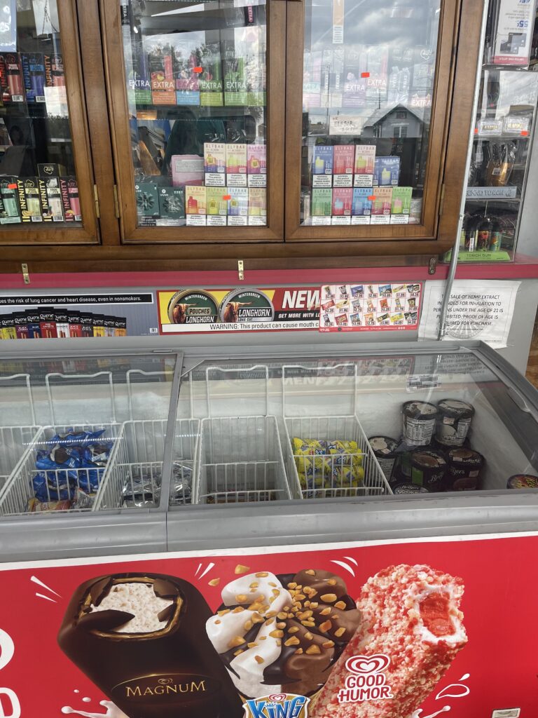 E-cig display and smokeless and cigar ads above an ice cream cooler 